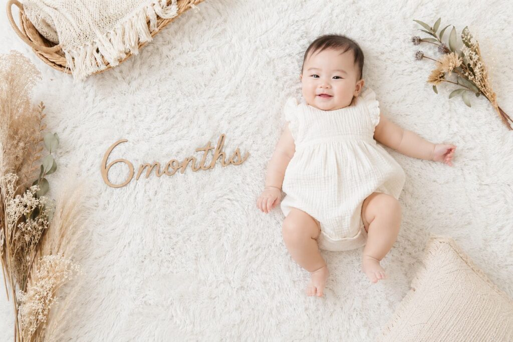 白いラグの上に寝かせた赤ちゃんと「6months」のレターバナー。ナチュラルで統一感のある色合い